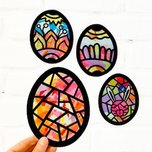 May include: Four oval-shaped decorations with black outlines and colorful, translucent stained-glass style patterns. One features a sun and hills, one has scalloped lines, one has a geometric mosaic, and one displays a pink rabbit face with long ears.
