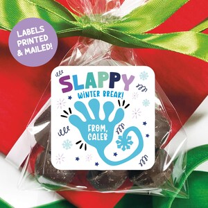May include: A clear cellophane bag filled with dark chocolate candies, tied with a green ribbon. A square label reads "SLAPPY WINTER BREAK!" with a blue hand graphic and the name "Caleb."