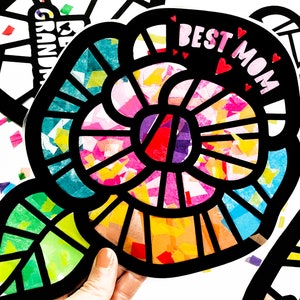 May include: A black paper craft flower with a colorful tissue paper design. The flower has a leaf and the words "Best Mom" are written on the flower.