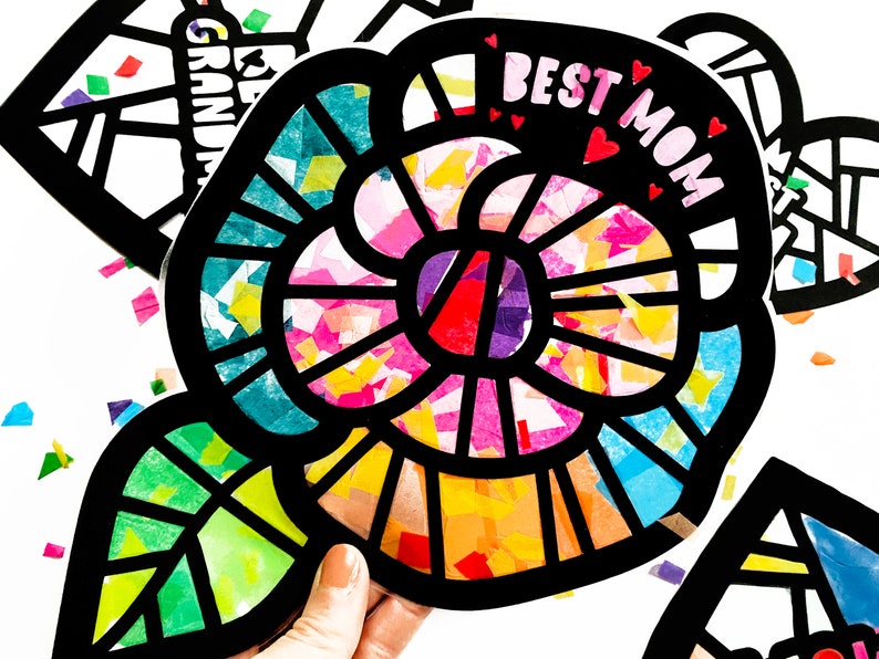 May include: A black paper craft flower with a colorful tissue paper design. The flower has a leaf and the words "Best Mom" are written on the flower.