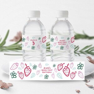 May include: Water bottle labels with a strawberry and floral design. The labels say "Ava is 3" and "Ava's Berry First Birthday".