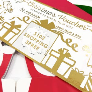 May include: A Christmas voucher with gold foil accents and the text "Christmas Voucher" and "Scratch to Reveal Your Gift". The voucher is addressed to Abraham and is from Mom & Dad. The scratch-off area reveals "$100 Shopping Spree".