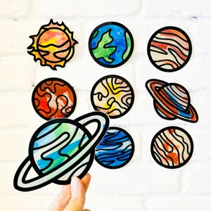 May include: Nine colorful paper planets with a variety of designs and patterns. The planets are all different sizes and shapes, and they are all surrounded by a white background.
