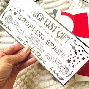 Pode incluir: Um vale-presente "Nice List Gift" para compras em prata e branco do Papai Noel. O certificado inclui texto e elementos decorativos como estrelas, renas e um selo do P&oacute;lo Norte. O certificado tem um valor de $150.