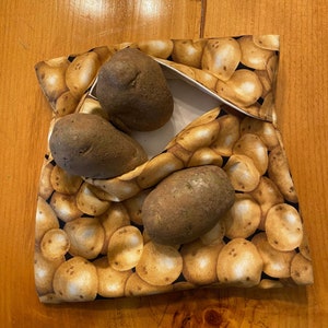 May include: A brown fabric bag with a potato print design. The bag is filled with four brown potatoes.