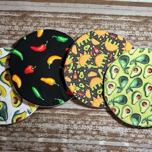 May include: Four round fabric coasters with different Mexican-themed designs. One coaster features avocados, another has green and red peppers, a third has avocados and tacos, and the last one has avocados on a green background.