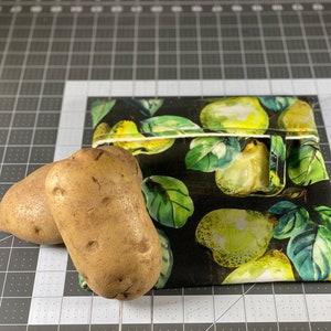 May include: Two brown potatoes next to a reusable snack bag. The bag is black with a pattern of green pears and leaves. The bag has a white zipper closure.