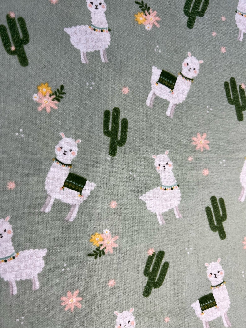 May include: A green fabric with a repeating pattern of white llamas, green cacti, and pink and yellow flowers.