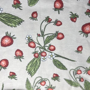 May include: A beige fabric with a repeating pattern of red strawberries and green leaves. The strawberries are in various stages of ripeness and some have white flowers.