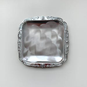 May include: A silver square serving tray with an ornate floral design around the edge.