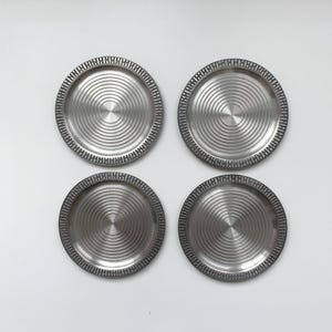 May include: Set of four silver-colored metal coasters with a concentric circle design.