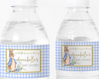 以下が含まれることがあります： 青いギンガムチェックのラベルが付いた透明なプラスチック製の水筒が2本。ラベルには、水彩画で描かれたウサギのイラストが描かれており、「A sweet little bunny is on the way」と「Annabelle's Baby Shower」と書かれています。
