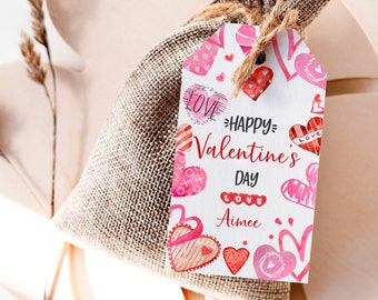 Könnte beinhalten: Ein weißes Geschenkanhänger mit rosa und roten Herzen und dem Text "Happy Valentine's Day" und "Aimee", befestigt an einem braunen Jutesack.