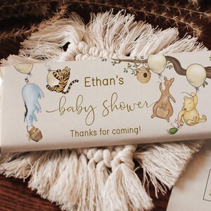 May include: A white chocolate bar wrapper featuring a Winnie the Pooh theme. The wrapper includes illustrations of Winnie the Pooh, Tigger, Eeyore, and Kanga. The text on the wrapper reads "Ethan's baby shower Thanks for coming!"
