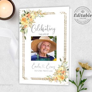 May include: A white memorial card with a gold frame and floral accents. The card features a photo of a woman wearing a straw hat and a floral print shirt. The text "Celebrating the life of Emilie & Evans July 15, 1962 - March 11, 2022" is printed on the card.