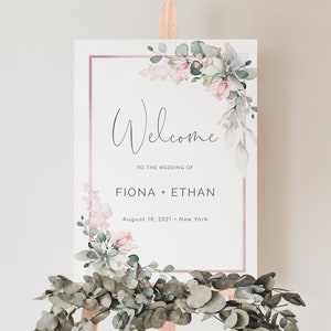 May include: A white wedding welcome sign with a pink and green floral design. The sign reads "Welcome to the wedding of Fiona + Ethan August 18, 2021 - New York".