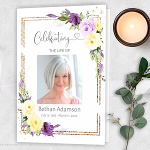 May include: A white memorial card with a gold glitter frame and purple and yellow flowers. The text "Celebrating the Life of" is at the top of the card. A photo of a woman is in the centre of the card. The text "Bethan Adamson July 15, 1962 - March 11, 2022" is below the photo.