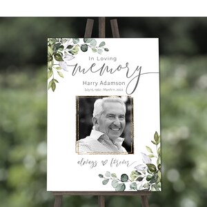 May include: A white memorial sign with a black and white photo of a man, surrounded by green eucalyptus leaves. The sign reads "In Loving Memory Harry Adamson July 15, 1962 - March 11, 2022 always forever".