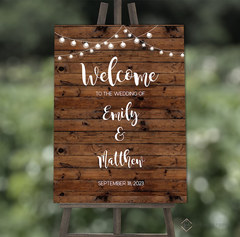 May include: Rustic wooden wedding welcome sign with white string lights, the text "Welcome to the wedding of Emily & Matthew September 18, 2023".