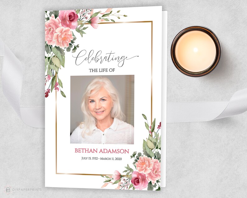 May include: A white memorial card with a gold frame and pink floral design. The text "Celebrating the Life of" is at the top of the card. A photo of a woman is in the center of the card. The text "Bethan Adamson" is below the photo, with the dates "July 15, 1932 - March 11, 2020".