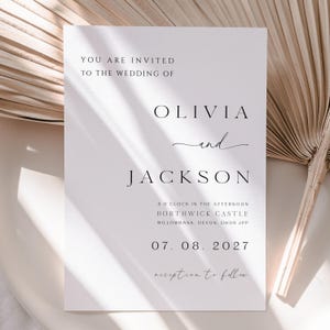 Op de afbeelding: Een witte trouwkaart met zwarte tekst die luidt: You are invited to the wedding of Olivia and Jackson, 3 o'clock in the afternoon, Borthwick Castle, Willowbank, Devon, DH09 JPP, 07. 08. 2027, reception to follow.
