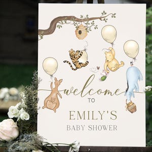 May include: A cream-coloured baby shower sign with illustrations of Winnie the Pooh characters. The sign includes the text "welcome to Emily's baby shower" in gold script, with balloons and a beehive.