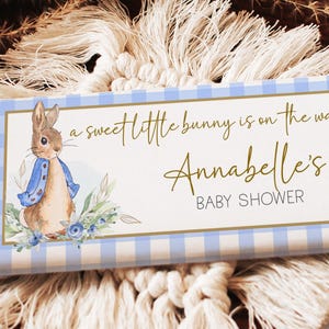 May include: A blue and white gingham patterned baby shower favor with a bunny illustration and the text "a sweet little bunny is on the way Annabelle's Baby Shower".