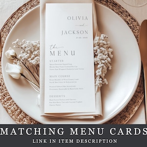 May include: A wedding menu card with the names Olivia and Jackson, and the date 21.05.2026, on a white plate with a gold fork and knife. The menu card is on a white napkin with floral accents. The text "The Menu" is visible.