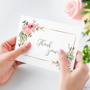 May include: A white card with a gold frame and pink floral accents. The card says "Thank you" in cursive.