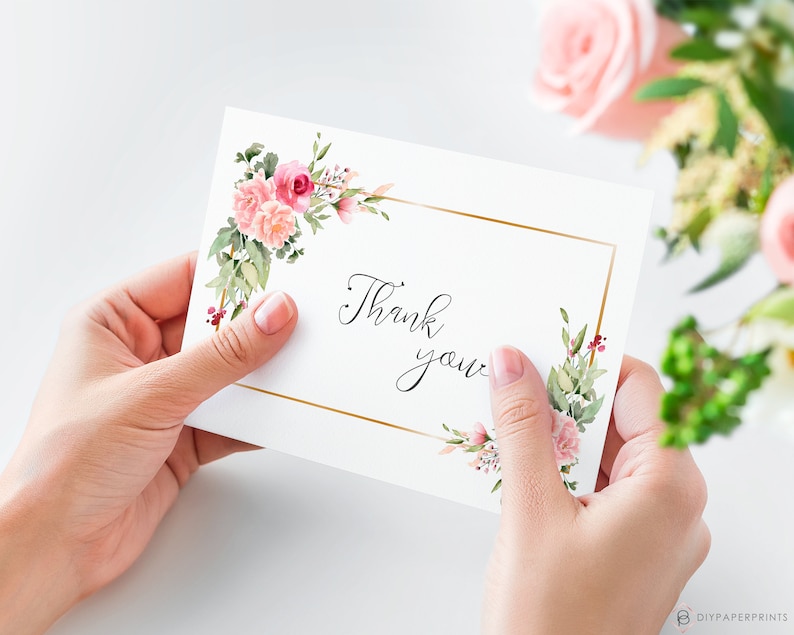 May include: A white card with a gold frame and pink floral accents. The card says "Thank you" in cursive.