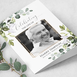 May include: A white card with a black and white photo of a man smiling. The card has a gold glitter border around the photo and green watercolor leaves on the sides. The text "Celebrating the life of Harry Simpson July 15, 1932 - March 11, 2022" is printed on the card.