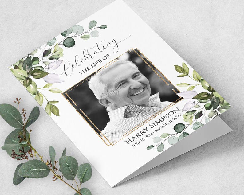 May include: A white card with a black and white photo of a man smiling. The card has a gold glitter border around the photo and green watercolor leaves on the sides. The text "Celebrating the life of Harry Simpson July 15, 1932 - March 11, 2022" is printed on the card.