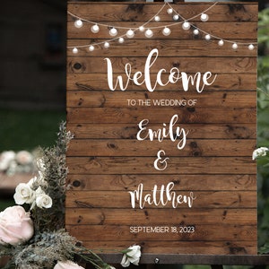 May include: Rustic wooden wedding welcome sign with string lights, featuring the text "Welcome to the wedding of Emily & Matthew" and the date "September 18, 2023".