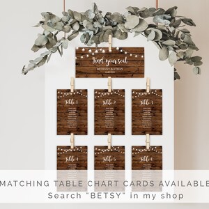 May include: Rustic wooden wedding seating chart cards with string lights. The cards are hung with clothespins and feature the text "Find your seat" and the names Bethany & Ethan. The cards are labeled with table numbers 1 through 6.