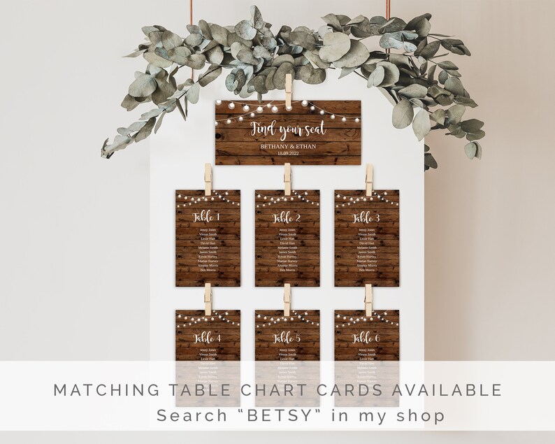 May include: Rustic wooden wedding seating chart cards with string lights. The cards are hung with clothespins and feature the text "Find your seat" and the names Bethany & Ethan. The cards are labeled with table numbers 1 through 6.