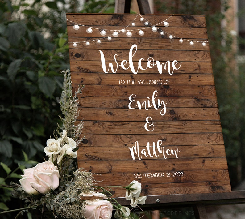 May include: Rustic wooden wedding welcome sign with string lights, featuring the text "Welcome to the wedding of Emily & Matthew, September 18, 2023".