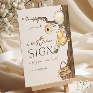 May include: A custom sign on a wooden easel, featuring a Winnie the Pooh illustration. The sign includes the text "custom SIGN" and "add your own text", with an 8 x 10 portrait format. The illustration shows Pooh Bear, Piglet, a beehive, and a honey pot.