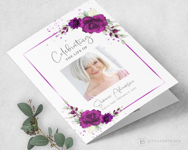 May include: A white folded card with a purple floral design and a photo of a woman. The text "Celebrating the Life of Simone Adamson July 15, 1959 - February 11, 2021" is printed on the card.