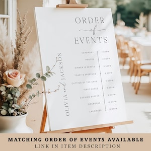 May include: A white wedding event sign on a wooden easel displays the order of events. The sign features elegant black text, including the names "Olivia and Jackson" and a detailed schedule with times for the ceremony, photos, dinner, and more. The bottom of the sign reads "MATCHING ORDER OF EVENTS AVAILABLE".