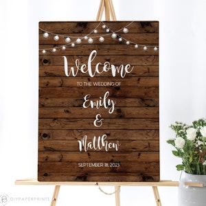 May include: Rustic wooden wedding welcome sign with string lights, featuring the text "Welcome to the wedding of Emily & Matthew, September 18, 2023".