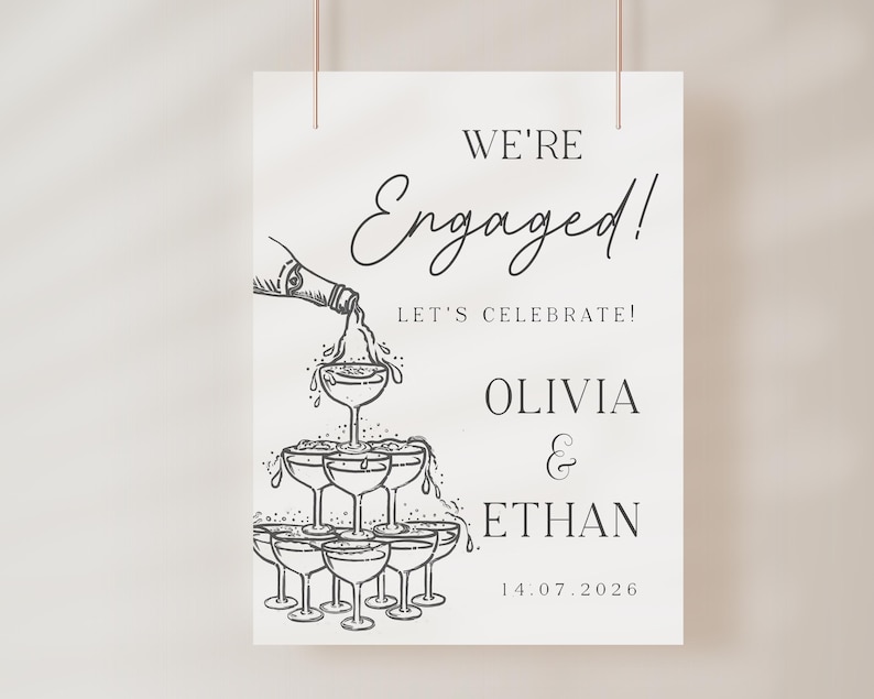 K&ouml;nnte beinhalten: Ein wei&szlig;es Schild mit den Worten "We're Engaged!" in eleganter Schrift, darunter "Let's Celebrate!". Eine Zeichnung zeigt Champagner, der in eine Pyramide aus Gl&auml;sern gegossen wird. Die Namen "Olivia & Ethan" und das Datum "14.07.2026" sind ebenfalls enthalten.