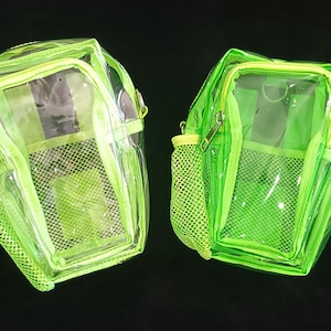 May include: Two neon green clear backpacks with yellow zippers and mesh side pockets. The bags have a transparent design, allowing visibility of the contents. The bags are designed with a small handle and adjustable straps.