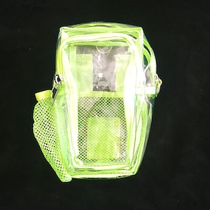May include: A clear, neon green backpack with a zippered main compartment and a mesh side pocket. The backpack has a rectangular shape with a top handle and adjustable straps. The bag is made of a transparent material, allowing visibility of the contents.