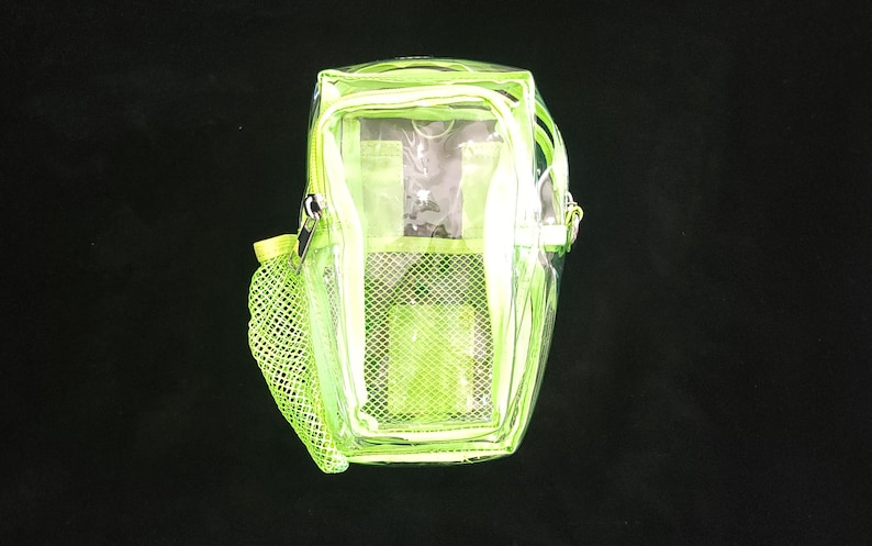 May include: A clear, neon green backpack with a zippered main compartment and a mesh side pocket. The backpack has a rectangular shape with a top handle and adjustable straps. The bag is made of a transparent material, allowing visibility of the contents.