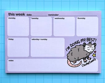 May include: A purple weekly planner with a reminder section and a cute cartoon possum illustration. The possum is gray and white with pink accents and says "I'm doing my best! (sometimes)"