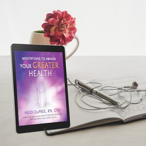 Pode incluir: Um tablet exibe a capa do livro "Meditations to Awaken Your Greater Health" de Heidi Dupree. Uma caneta, fones de ouvido, um caderno e uma caneca com uma flor vermelha também estão visíveis. A capa do livro tem um fundo roxo e branco.