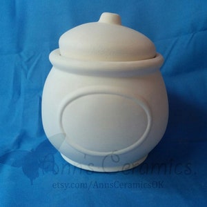 May include: White ceramic jar with a lid and a round, raised design on the front. The jar is blank and ready to be painted.