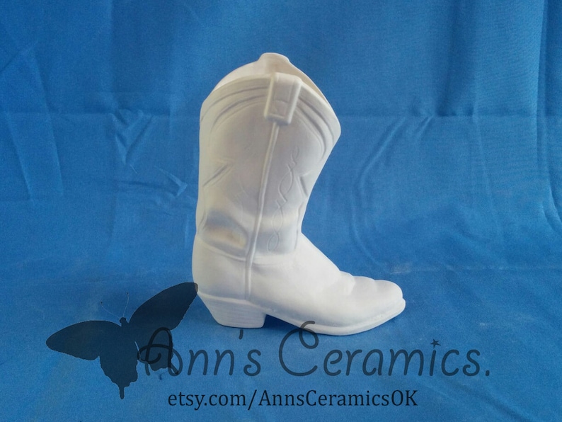 May include: White ceramic cowboy boot shaped planter. The boot is a traditional style with a pointed toe and a high heel. The boot is unpainted and ready to be decorated.