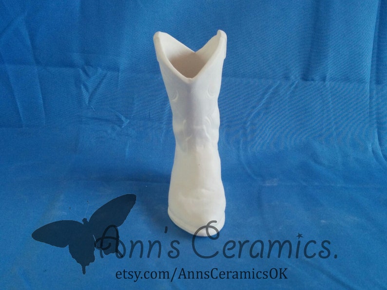 May include: White ceramic cowboy boot shaped vase. The boot has a pointed toe and a decorative design on the side.  Ann's Ceramics. etsy.com/AnnsCeramicsOK