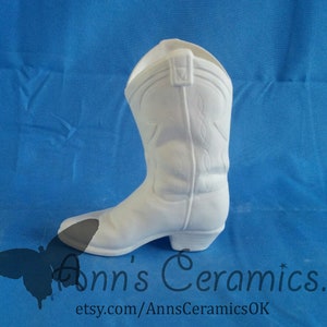 May include: White ceramic cowboy boot planter. The boot is a traditional style with a pointed toe and a high heel. It is a great way to add a rustic touch to your home decor.